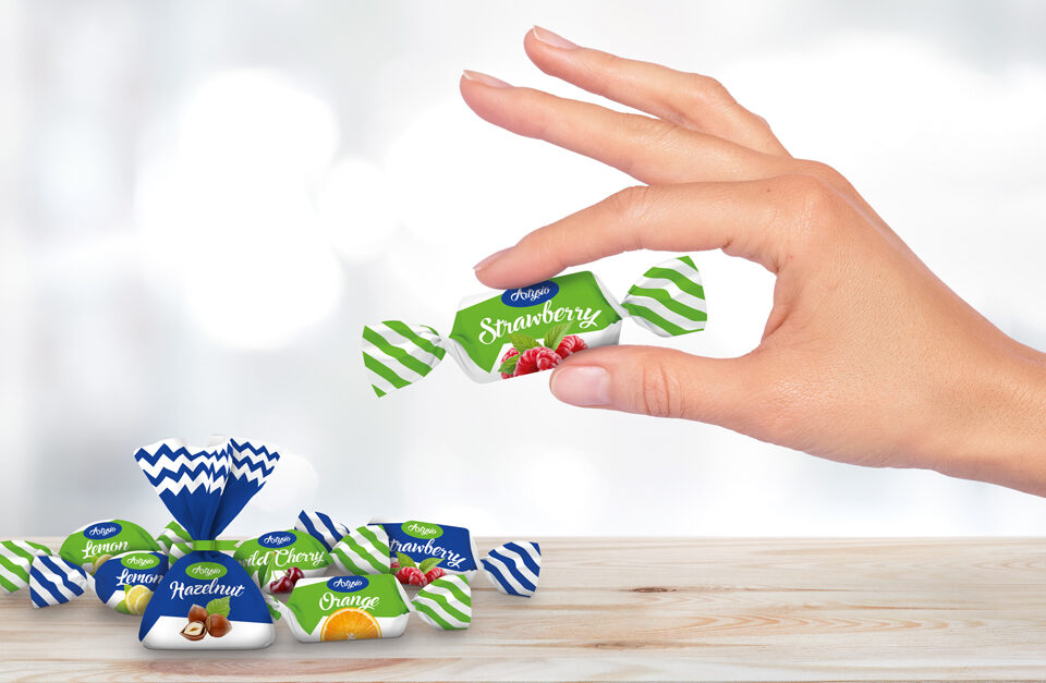 Bonbons in buntem Papier auf Holzplatte vor grauem Hintergrund