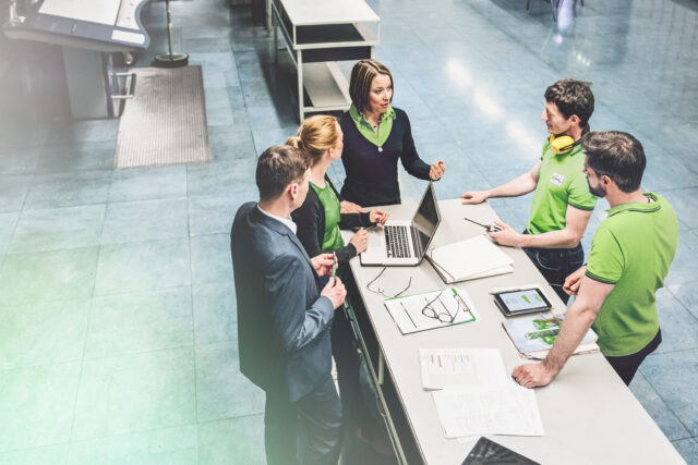 Drei Männer und zwei Frauen stehen um einen Tisch und halten ein Meeting ab