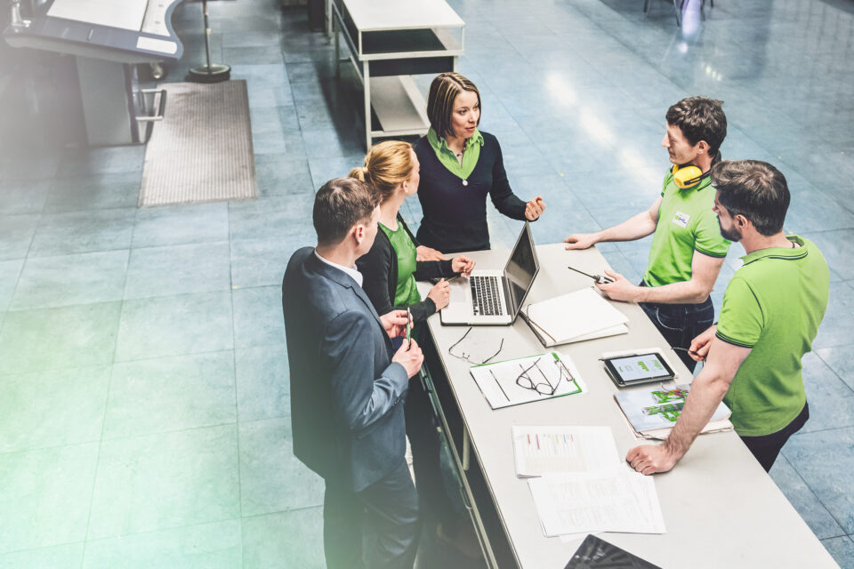 Drei Männer und zwei Frauen stehen um einen Tisch und halten ein Meeting ab